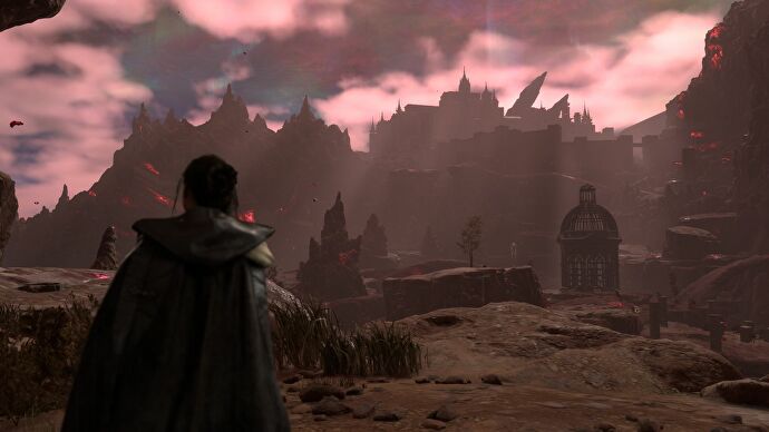 Frey, protagonist of Forspoken, stands looking at a forbidding black and gray rocky landscape, a castle off in the distance.  There are red clouds in the sky, and red particles floating in the air