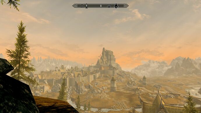 An evening vista in The Elder Scrolls V: Skyrim, at golden hour, showing the plains town of Whiterun, surrounded by windmills